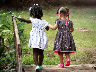 Two girls, holding hands, walk across a bridge.