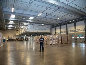 A man stands in a warehouse with lots of boxes behind him.