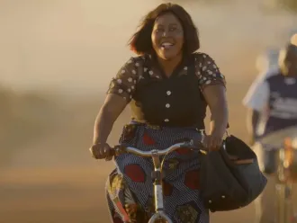 A woman with a book bag rides a bicycle down a street 