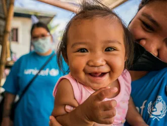 Gros plan sur une petite fille souriante tenue par un membre du personnel de l’UNICEF aux Philippines.