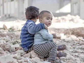 Two children sit in the rubble of their former home.
