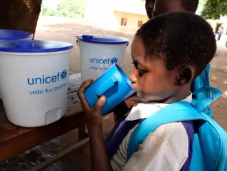 A student drinks from a cup with a UNICEF logo.