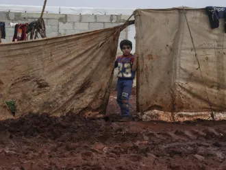 Young boy stands near the tent where he lives with his family, Atma camp, Idlib