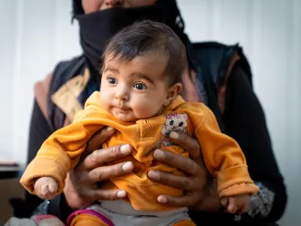 A baby waits to receive new winter clothes in Zaatari Refugee Camp, Jordan.