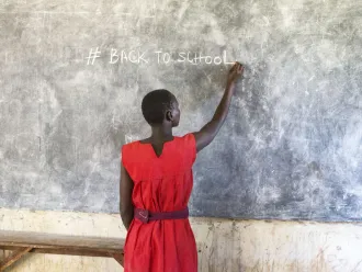 A girl writes on a chalkboard in a classroom in Uganda.