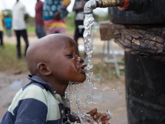 A child drinks from a water point at the Samora Machel II accommodation centre.
