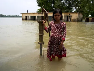 A little girl stands near a flooded water pump in India.
