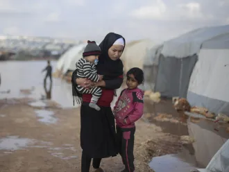 On 19 January 2021, families stand outside of tents in a flooded area of Kafr Losin Camp in northwest Syrian Arab Republic.