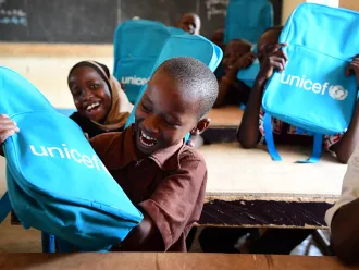 Au Niger, des élèves enthousiastes sourient et rient à leur pupitre après avoir reçu des sacs à dos de l’UNICEF remplis de fournitures scolaires.