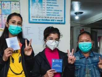 Three female health workers give the 'v for vaccinated' sign outside a clinic in Nepal.