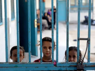 Three girls peeking outside a gate at one of 29 UNRWA schools used as temporary shelter.