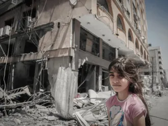 On 17 May 2021, a Palestinian girl stands in front of their home as her family extracts their possessions from inside their damaged home after being targeted in Gaza City.