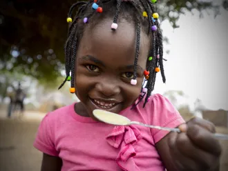 A child smiles as she eats a meal at the school in Mbuene village, Magude district, Maputo Province, Mozambique
