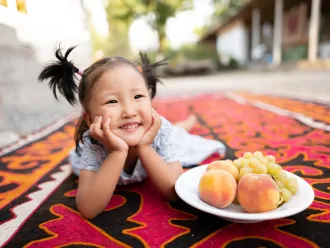 A little girl poses with a bowl of fresh fruits.