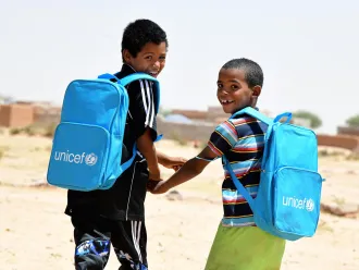 Dans le nord du Niger, deux enfants rient et marchent ensemble en portant leurs nouveaux sacs à dos de l’UNICEF remplis de fournitures scolaires.