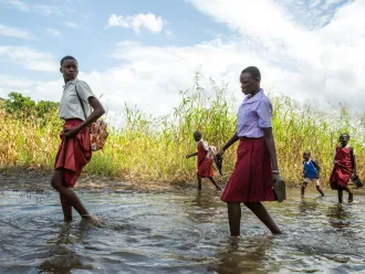 Students walking on foot across flooded paths - South Sudan