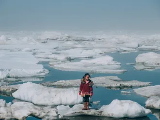 Alaska, United States: a girl wearing a red coat stands on an ice floe.