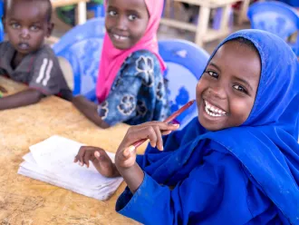 De jeunes élèves rient en faisant leurs devoirs ensemble à une table dans une classe d’une école primaire de Dolow, en Somalie.