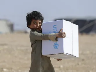 A child holds a UNICEF box, in the background out of focus you can see tents