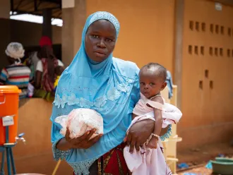 a woman in a blue scarf holding a packet of food in one hand and a child in the other. 