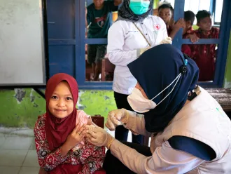 A girl looks at the camera as a nurse administrators an injection to her arm. 