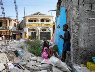 On 18 July 2022 in Les Cayes, Haiti, children play in the rubble of homes destroyed in the 2021 earthquake. The girl in blue lives nearby with her mother, Yolande Felix, and younger sister, Valentine.