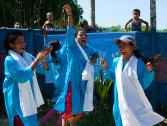 Three girls cheer on the sidelines of a soccer game in Bangladesh. 