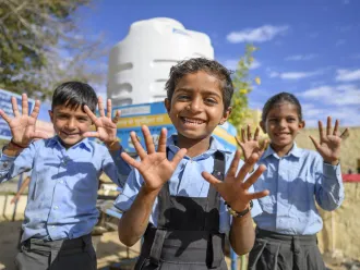 Three children showing their washed hands smile at the camera.