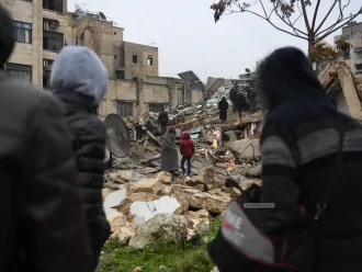 People gather around collapsed buildings as rescue teams look for survivors following an earthquake in the Syrian city of Aleppo