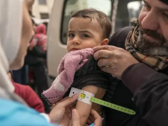 On 10 February 2023, Sondos, two years and eight months, in her father’s arms, is screened for malnutrition by a UNICEF-supported mobile health team worker, using a mid-upper arm circumference (MUAC) tape, in the Alsalheen neighbourhood, Aleppo city, north Syria.