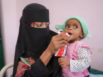 On 23 February 2023 in Aden, Yemen, 16-month-old Rowaida Raeed Ali Hasan is fed a sachet of Plumpy ‘Nut ready-to-use therapeutic food (RUTF) by her mother, Gouma’a Mohammed Hasan Abdullah. Rowaida is being treated for severe acute malnutrition in the Therapeutic Feeding Centre at Al Sadaqa Hospital.