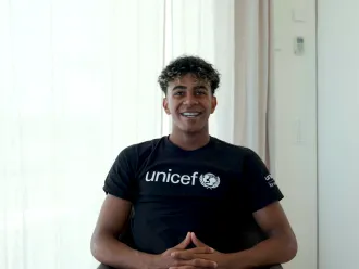 A young man in a black unicef tshirt looking at the camera and smiling. 