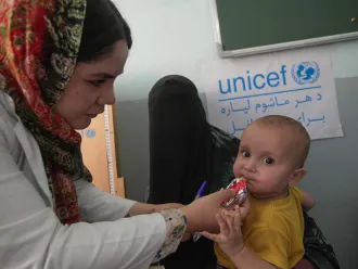 A health worker feeds a child ready-to-eat therepeutic food while his mother holds him 