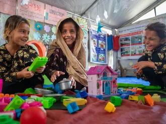 In a tent, three girls laugh and play with toys.
