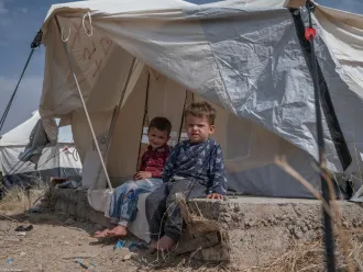 Syrian child sit outside a makeshift tent in Iraq