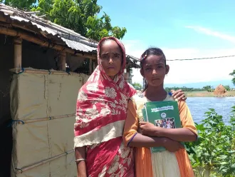 A woman and her daughter stand outside a makeshift home in Bangladesh.