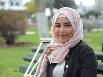 Nour sitting on a bench with her crutches beside her.