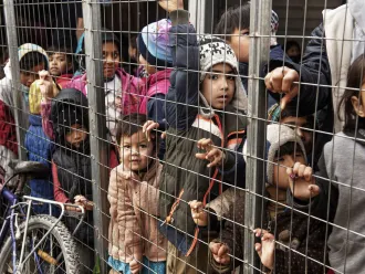 Children wait in a crowded processing area for refugees.
