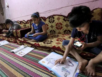 Children study using recorded lessons at a refugee camp.