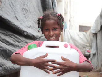 A little girl holds a jerry can of clean water.