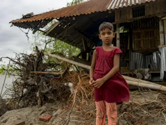A child stands in front of her tin house in Bangladesh.