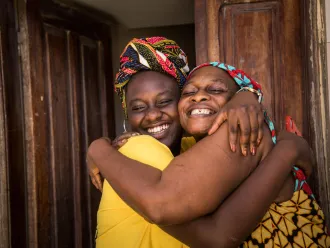 A mother and daughter hug outside their home.