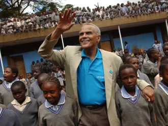 UNICEF Goodwill Ambassador Harry Belafonte waves to onlookers, standing amidst a crowd of children at the Kihumbuini primary school in Kangemi, a poor neighbourhood in Nairobi, the capital.