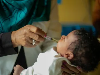 A hand administers a vaccine to a baby, using a plastic syringe.