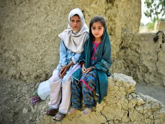 Muriko bibi (7) and Tehseen (6) sit on the damaged wall of their mud house which was almost destroyed during the 2022 floods in Pakistan.