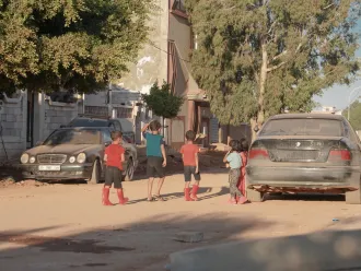 Young children are walking around in the neighborhood in boots despite the hot weather because they still worry about the floods and drowning, they have been displaced to a whole new city that they are still trying to familiarize themselves with.