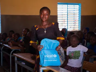 Une fille tient un sac à dos UNICEF bleu en avant d'elle. Derrière elle se trouve une dizaine d'étudiants.
