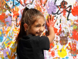 At a UNICEF-supported hub in Türkiye, a smiling girl puts her painted hands on a wall of colourful handprints. 