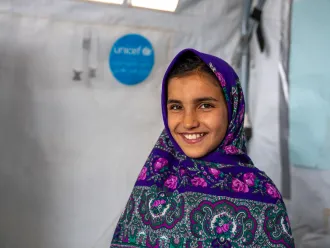 Girl in a headscarf smiling inside a UNICEF-supported learning space in Herat, Afghanistan.
