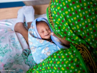 Un bébé enveloppé dans une serviette sourit sur les genoux de sa mère.